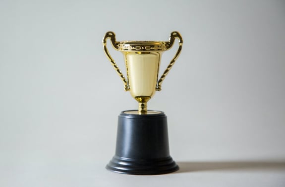 A golden cup trophy award photographed against a white wallpaper. 