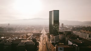 Aerial view of Zurich cityscape with modern glass skyscraper, busy highway, and distant mountains under hazy sky