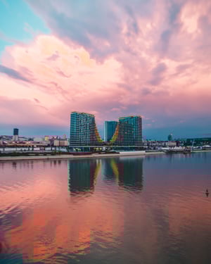 Modern residential towers in Belgrade waterfront at sunset with keylight illuminating buildings, pink sky reflected in calm river